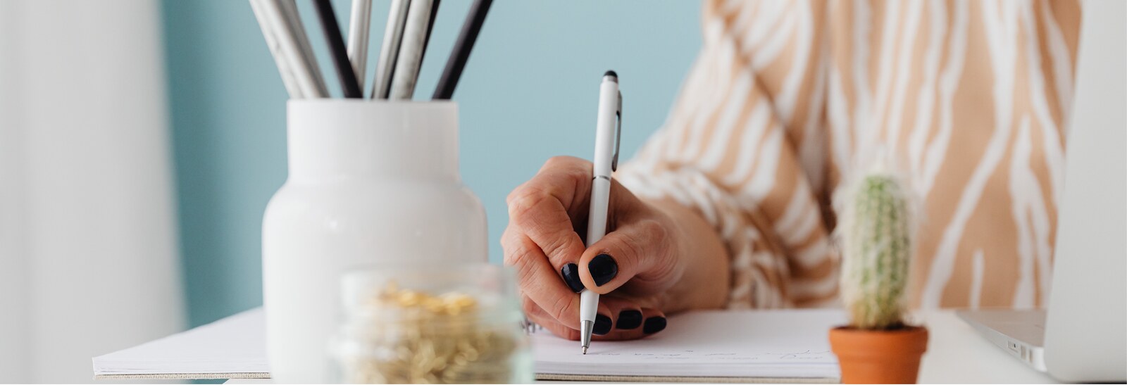 Mani che scrivono appunti alla scrivania, con cactus e vasi in ceramica